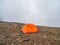 Summer camping in foggy mountain. Alpine landscape with orange tent at very high altitude with view to high mountain in dramatic