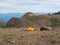 Summer camping in mountain. Bright alpine landscape with vivid orange tent at very high altitude with view to high mountain and