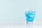 Summer cold blue lagoon drink with ice cubes in elegant shot glass on pastel mint background.