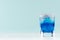 Summer cold blue lagoon drink with ice cubes, salt rim in elegant shot glass on pastel mint background.