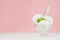 Summer cold dessert - three creamy ice cream balls in elegant glass bowl with green mint, silver spoon on white wood table.