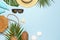 Summer composition flat lay. Round trendy rattan bag straw hat sunglasses tropical palm leaves coconut sunscreen seashells on blue