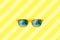 Summer concept image: yellow sunglasses with palm tree reflections isolated in large yellow striped background.