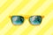 Summer concept image: yellow sunglasses with palm tree reflections isolated in pastel yellow striped background