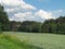 Summer countryside hilly landscape with emerald green meadow, woody hills on horizon and dramatic clouds in the sky