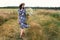 Summer in countryside. Stylish young woman in blue vintage dress and hat walking with white wildflowers in summer meadow. Happy