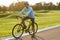 Summer cycling training. Young athletic man in sportswear riding bicycle along a road in city park at sunset, full