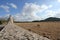 A summer day shot of an old stone cross on the side of a country road with a field with sheep, a hill, a blue sky with white