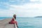 Summer Day. Smiling women relax and wearing red dress fashion sitting on the wooden bridge over the sea, blue sky background.