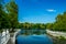 Summer day time park landscape walking district area waterfront fence by marble palisade along river stream, green trees foliage