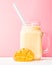 Summer drink mango milkshake in mason jar with drinking straw decorated with a half of mango on blue background
