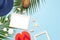 Summer fashion flat lay. Blue hat coral flip flops tropical palm leaves sunscreen white photo frame coconut seashells starfish on