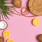 Summer fashion flat lay. Round trendy rattan bag, tropical palm leaves, coconut, orange on pink background. Top view, copy space.