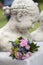 Summer flower bouquet with small roses in front of a small bust of a woman