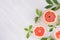 Summer fresh background - round slices pink grapefruits and green leaves on white wood board, top view, copy space.