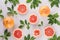 Summer fresh background - round slices pink grapefruits and green leaves on white wood board, top view, pattern.