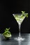 Summer fresh cocktail with lime slices, crushed ice and mint leaves in a martini glass backlit on black background