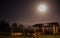 Summer full moon over lodge cabin and trees on foggy mountain highland