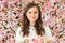 Summer happy brunette woman with cute smile holding flower gift and posing on pink floral background. Blooming, love, 8 march