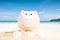 Summer happy piggy bank on sand beach over blurred tropical blue sea background