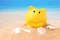 Summer happy piggy bank on white sand beach with blue sea on day noon light.