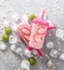 Summer heat: refreshing pink fruit ice with strawberry pieces surrounded by transparent and green ice cubes on a gray table.