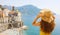 Summer holiday in Italy. Back view of young woman holding her hat with Atrani village on the background, Amalfi Coast, Italy