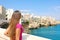 Summer holidays in Apulia. Back view of beautiful young woman in Polignano a mare town on Mediterranean Sea, Italy