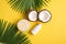 Summer holidays concept. Top view photo of white sunscreen bottle cream jars cracked coconuts and palm leaves on isolated yellow b