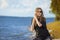 Summer Holidays and vacations.  Relaxing Caucasian Blond Female Girl in Street Clothing Posing Outdoors While Sitted On Shoreline