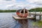 Summer lake nature landscape view of a traditional scandinavian water floating red wooden sauna spa next to a jetty.