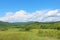 Summer landscape with green grass, hills road and clouds