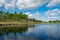 Summer landscape with lake and white cloud reflections in the water, tree silhouettes reflect in the lake water