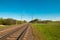 Summer landscape: old blue sky and clouds, green grass and trees, railway path road and old rusty industrial metal construction. A