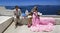 Summer love. Beautiful happy young couple in wedding clothes is posing near Church of the Three Bells in Fira in Santorini.