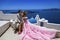 Summer love. Beautiful happy young couple in wedding clothes is posing near Church of the Three Bells in Fira in Santorini.