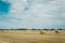 Summer meadow with yellow golden bales of hay bale in the stubble field. Agricultural field and a blue sky with clouds