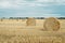 Summer meadow with yellow golden bales of hay bale in the stubble field. Agricultural field and a blue sky with clouds