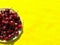 Summer mockup with red cherries on plate on yellow background close-up. Copy space