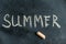 SUMMER. The name of the season is written in yellow chalk on a black chalkboard. Handwritten text. A piece of colored chalk lies