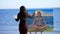 Summer, near river, on the beach. at sunrise, a beautiful woman artist in a tight suit draws a picture. god Shiva is