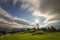 Summer night mountain panorama. Old wooden weathered shepherd huts on green clearing on cloudy evening sky background, bright road