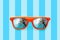 Summer orange sunglasses with palm trees reflections isolated in pastel blue background with stripes