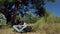 Summer outdoor recreation. A tourist under pine tree takes a book out of his backpack and reads.