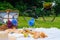 Summer picnic on sunny day with bread, fruit, bouquet hydrangea flowers, glasses wine, hat, book. Picnic basket on grass with food
