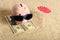 Summer piggy bank standing on towel from greenback hundred dollars with sunglasses on the beach and red parasol