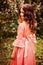 Summer portrait of curly smiling child girl in pink fairytale princess dress in the forest