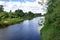 Summer river village landscape. Sandy beach on bank, green grass and trees blue river and cloudy sky