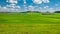 summer rural landscape. agricultural hilly field with a small hamlet, covered with green grass under a blue cloudy sky