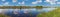 Summer rushy lake panorama view with clouds reflections